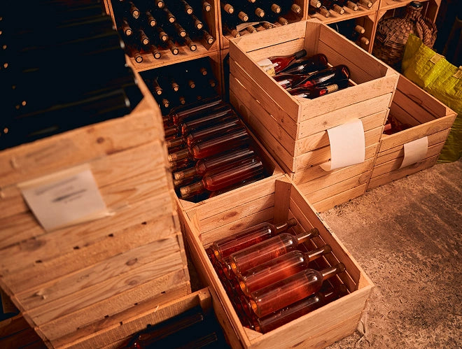 Wooden crates filled with bottles of red wine on a stone surface.